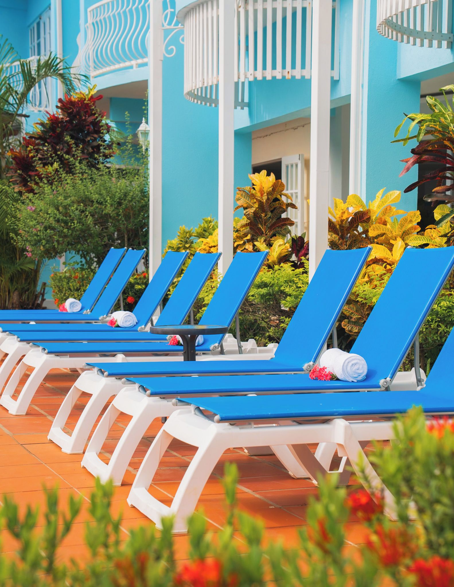 A row of blue lounge chairs with white frames, arranged on a tiled patio area.