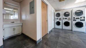 A laundry room with four front-loading washers and dryers, a wooden door, and a mirror above a white vanity with a sink. - King City Motel by OYO Pasco (Pasco)