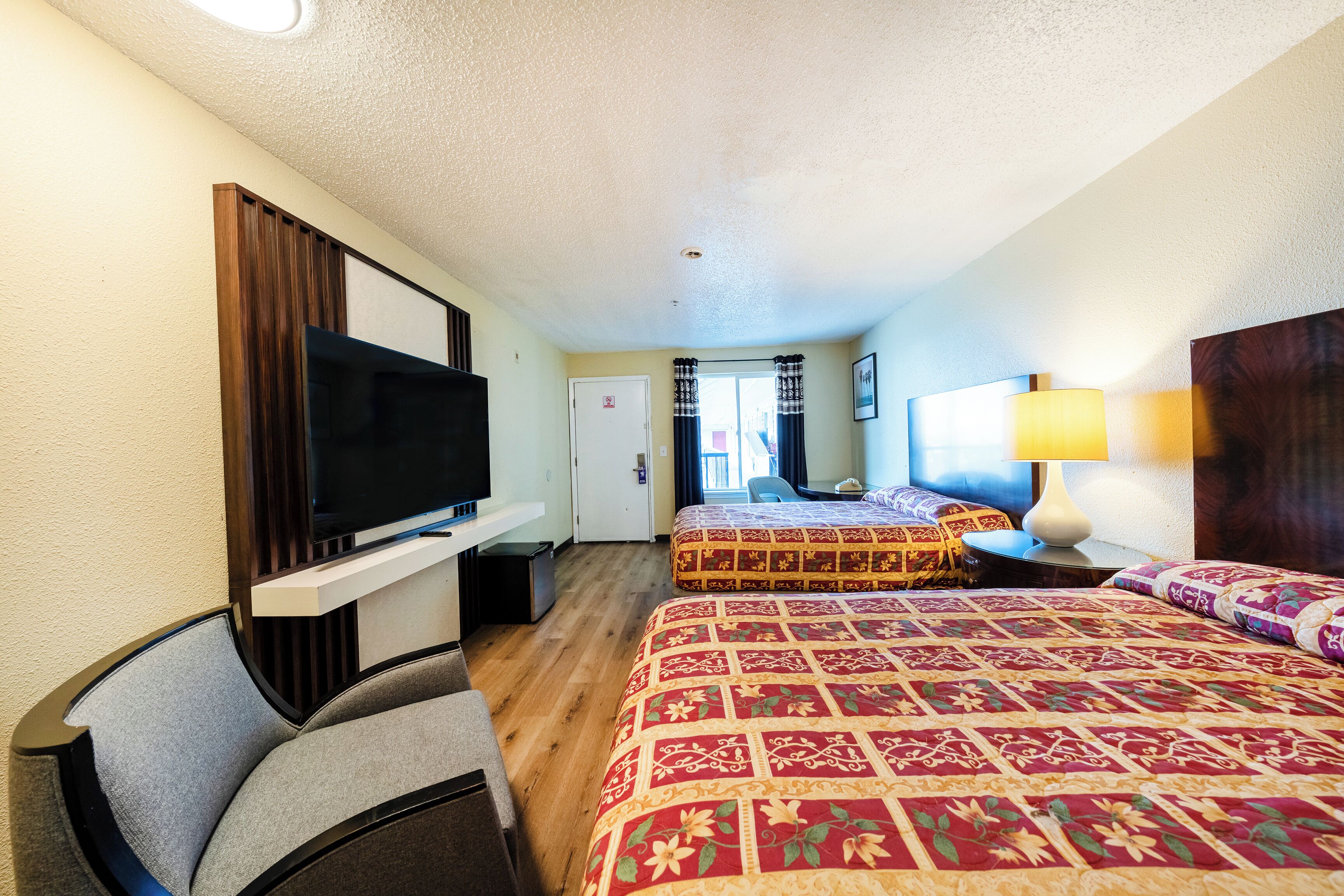 A hotel room with two beds, a TV, a desk, and a lamp.