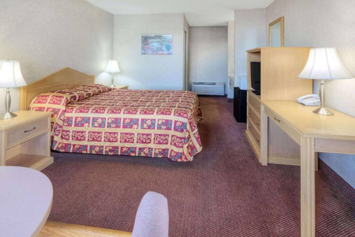 A hotel room with a bed, bedside tables, a desk, a chair, and a TV.
