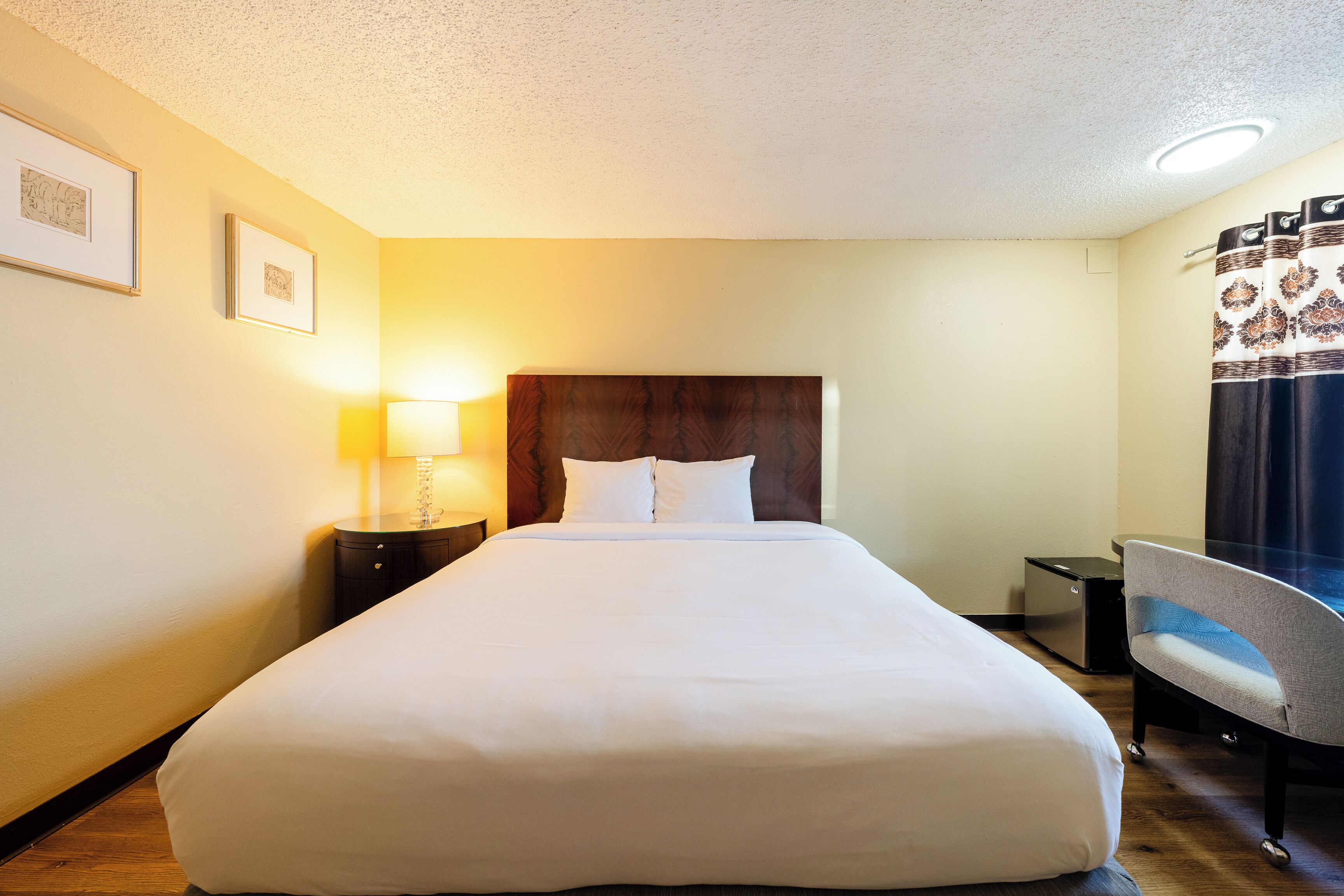A hotel room with a large bed, a desk, a chair, a lamp, and framed pictures on the wall.