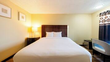 A hotel room with a large bed, a desk, a chair, a lamp, and framed pictures on the wall.