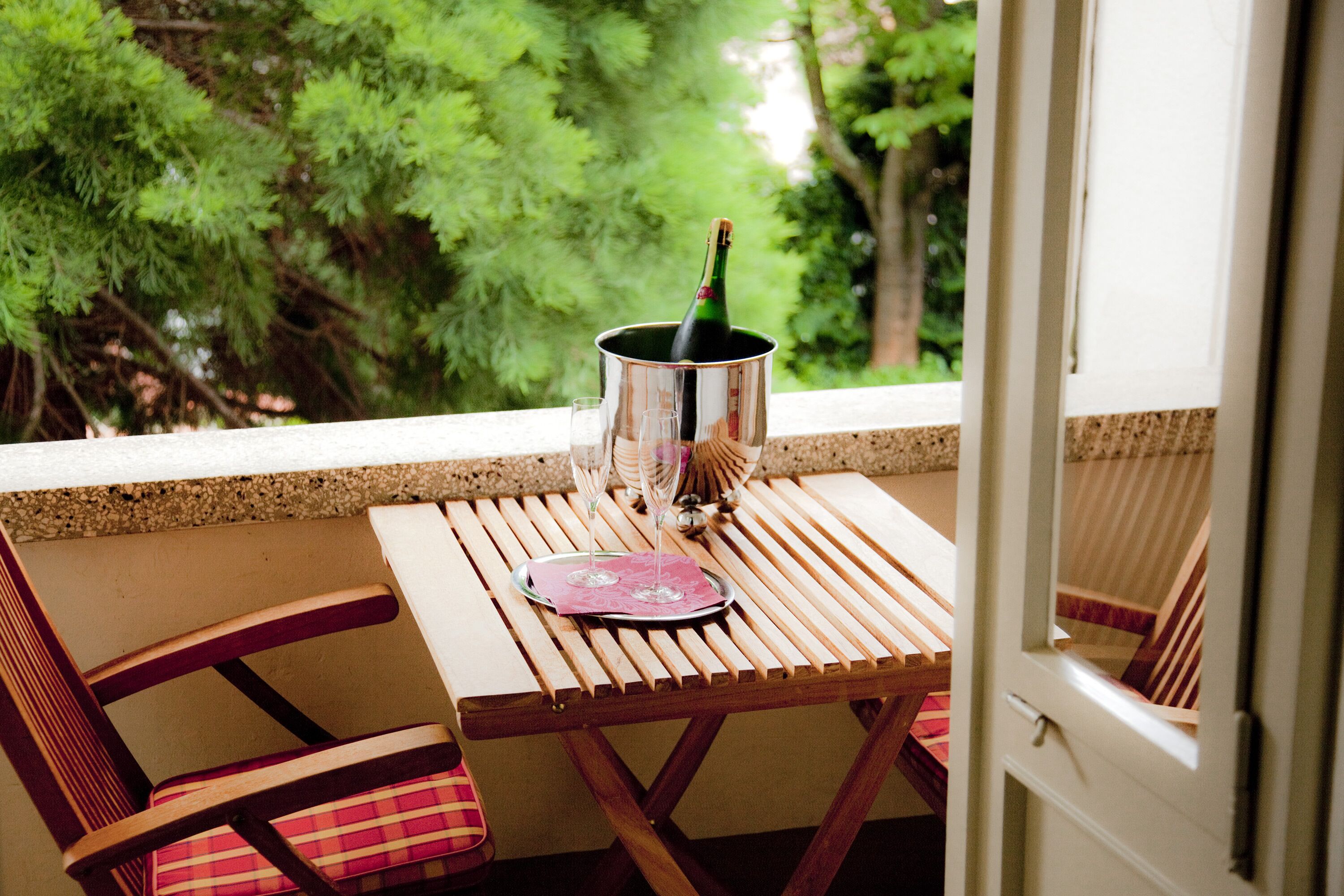 Ein Balkon mit Holztisch, zwei Stühlen und einer Champagnerflasche in einem Metallkübel.
