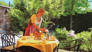 Un tavolo apparecchiato all'aperto con tovaglia gialla, circondato da sedie, e una persona che serve del cibo.