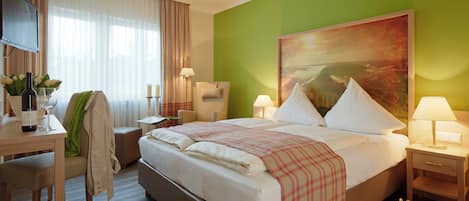 Una camera d'albergo con un letto, comodini, una scrivania, una sedia, una televisione e un quadro appeso al muro.