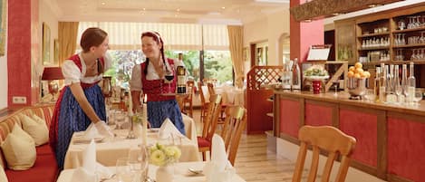 Un comedor con una mesa dispuesta para dos personas, un bar con varias botellas y vistas a zonas verdes al exterior.