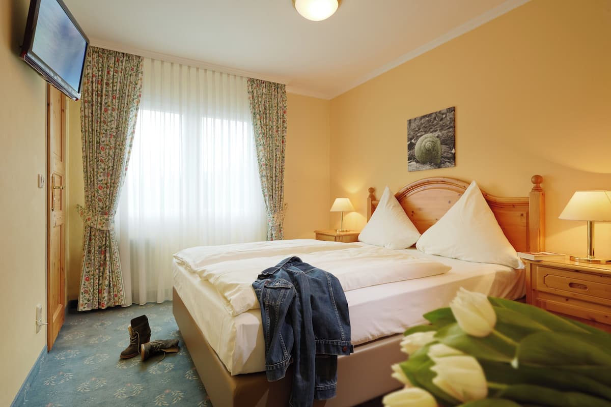 A hotel room with a bed, two bedside tables with lamps, a television on the wall, and a window with curtains.