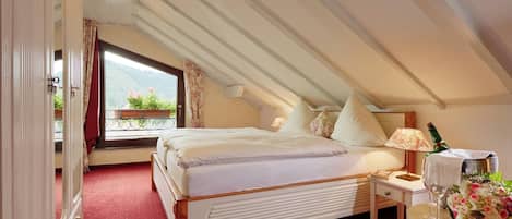 A bedroom with a large bed, a bedside table with a lamp, a bottle of champagne, and a bouquet of flowers.