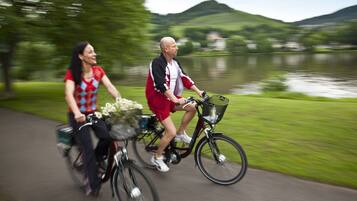 Two people riding bicycles on a path beside a lake with hills in the background.