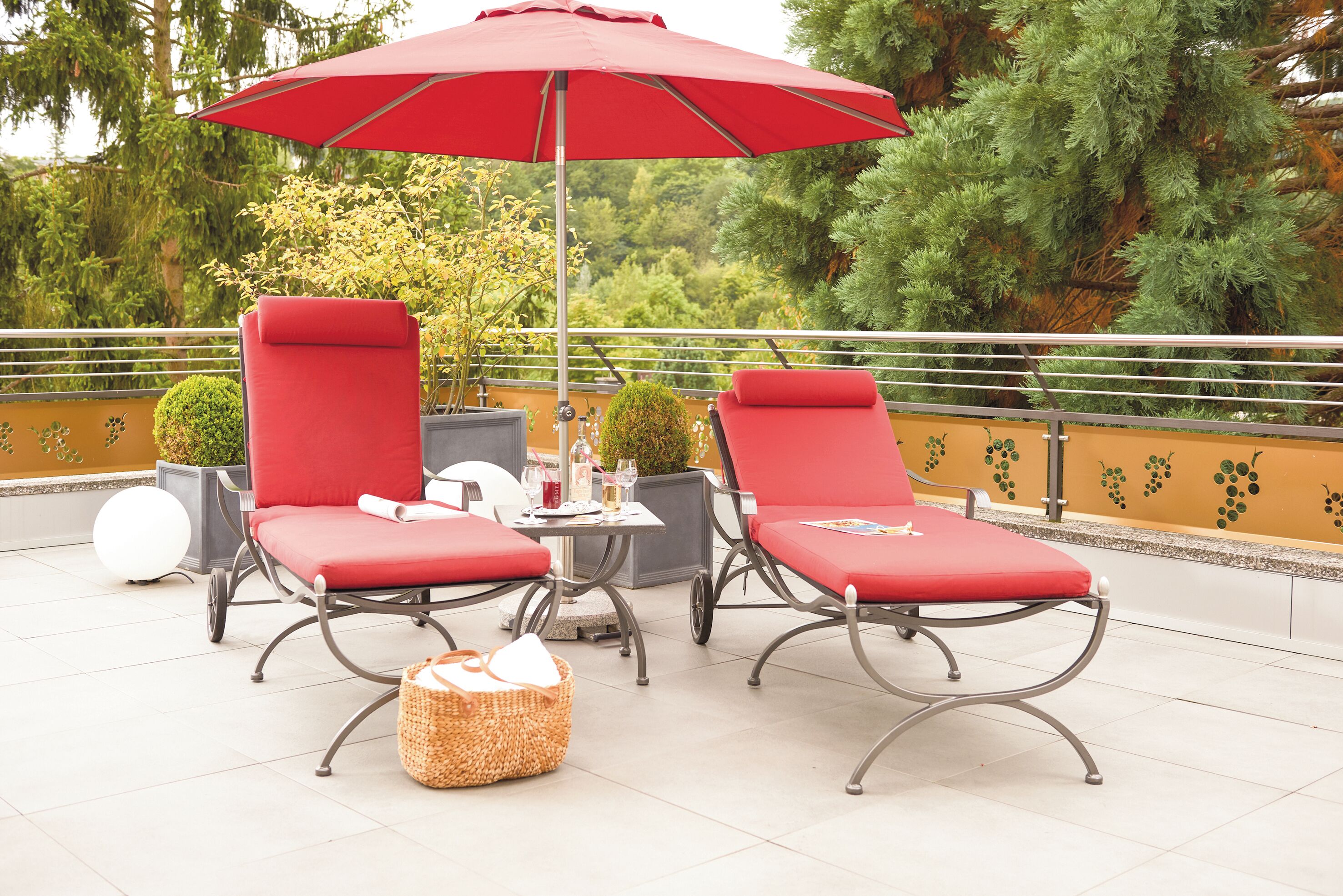 A terrace with two red lounge chairs, a table with drinks, and a red umbrella.