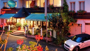 Un hotel con posti a sedere all'aperto, un cartello con la scritta 'BOMERS' e un'auto bianca parcheggiata di fronte.