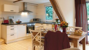 Una cucina con mobili bianchi, soffitto in legno, una finestra con tende e un tavolo da pranzo con sedie.