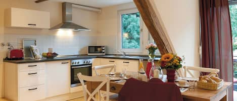 A kitchen with white cabinets, a wooden ceiling, a window with curtains, and a dining table with chairs.