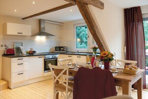 Una cocina con armarios blancos, techo de madera, una ventana con cortinas y una mesa de comedor con sillas.