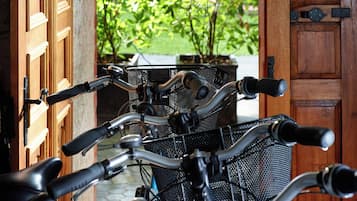 A row of bicycles parked in front of a wooden door with a view of a green garden.