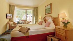 Una camera d'albergo con un letto grande, un comodino in legno, una poltrona in vimini, un tavolo con un vaso di fiori e un quadro appeso al muro.