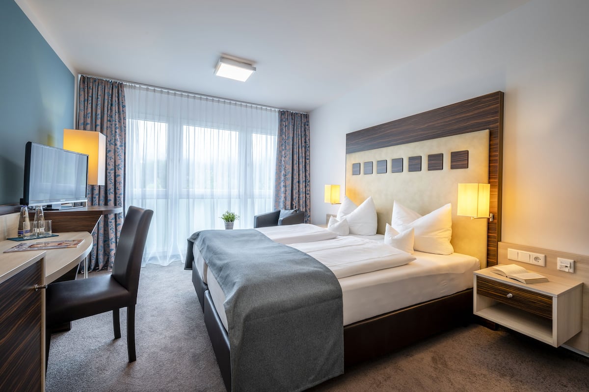 A hotel room with a large bed, a desk with a chair, a TV, and a window with curtains.