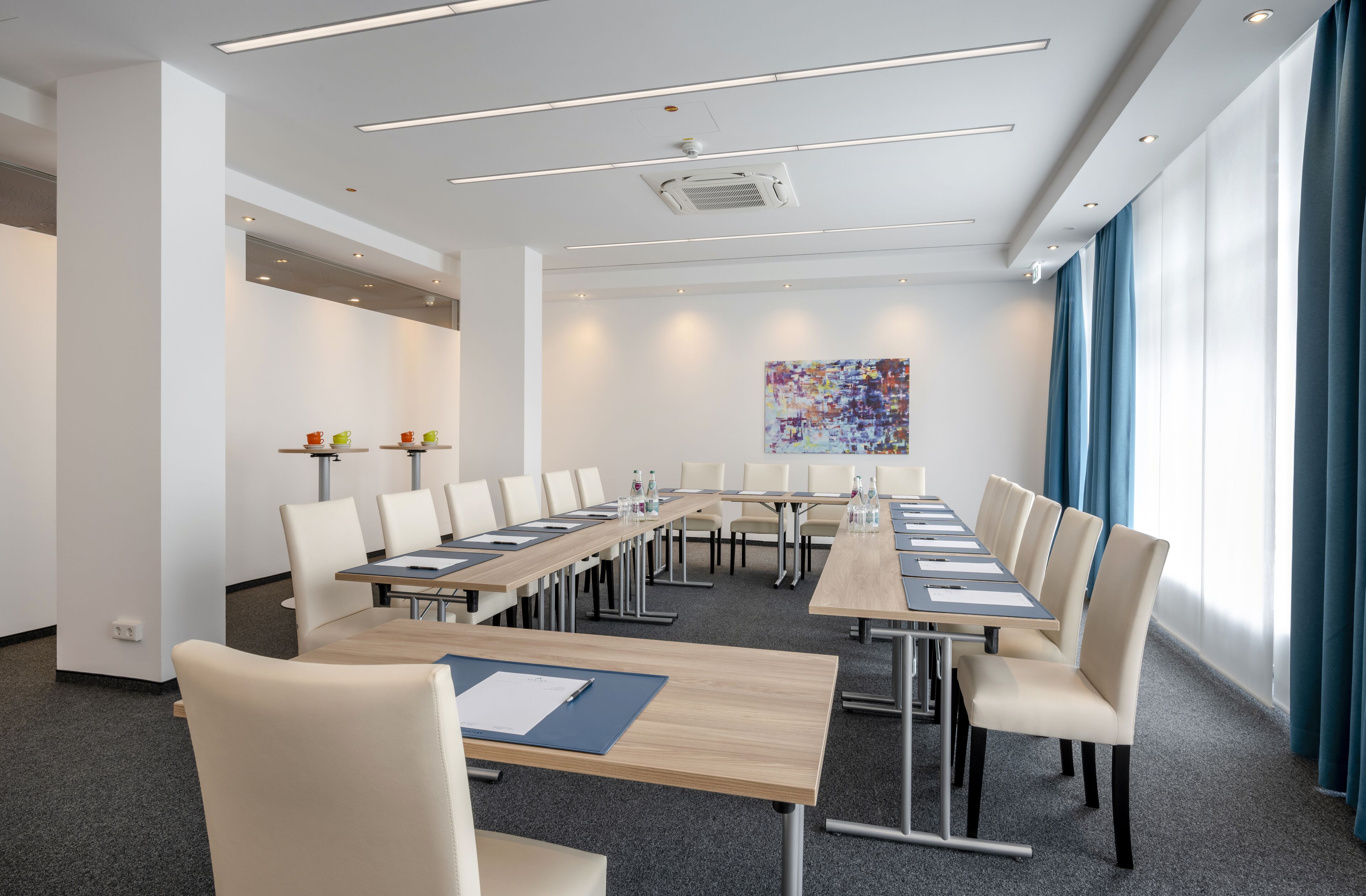 Un salón de conferencias con una mesa larga, sillas y un ventanal con cortinas.