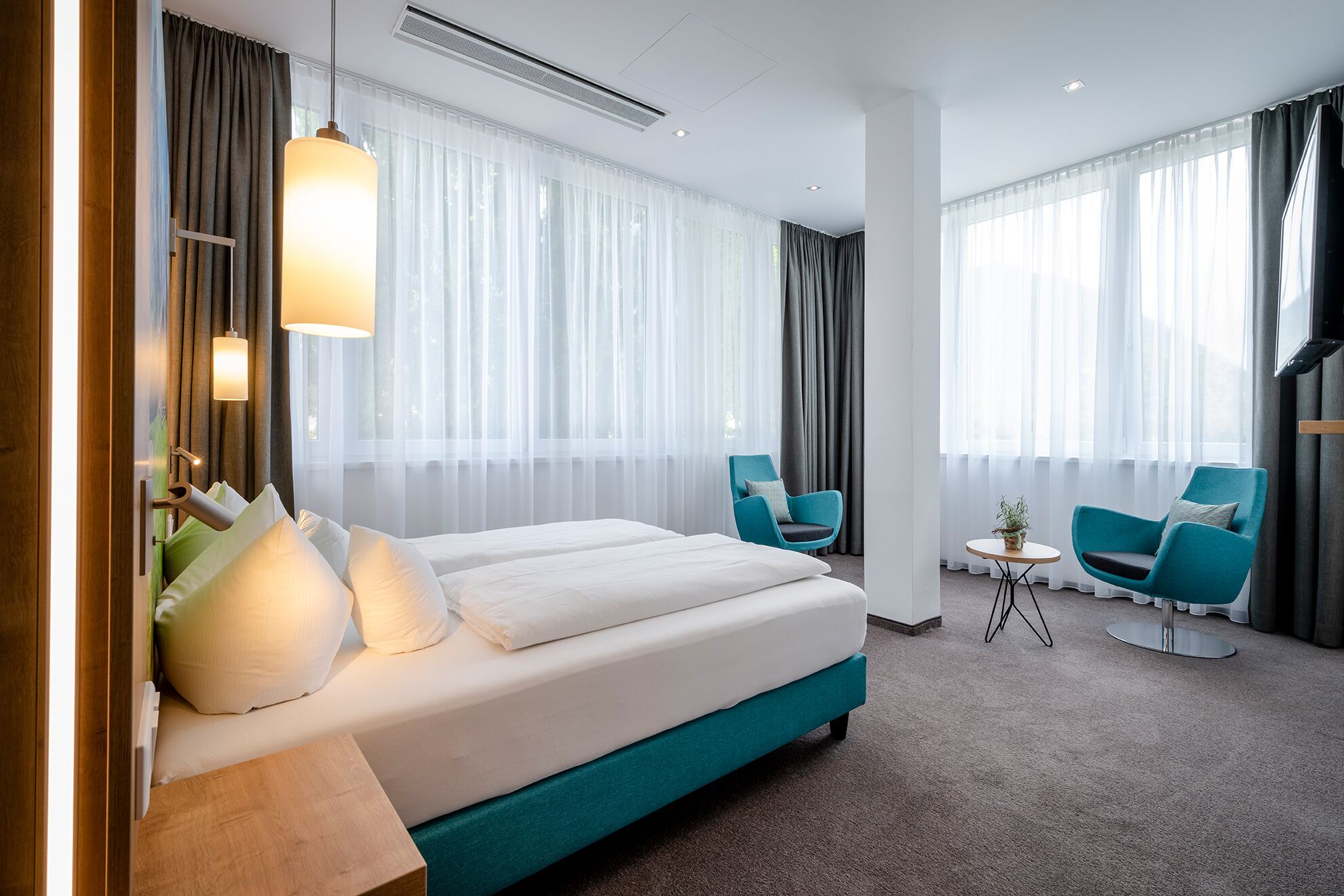 A hotel room with a large bed, two chairs, a small table, and a TV.