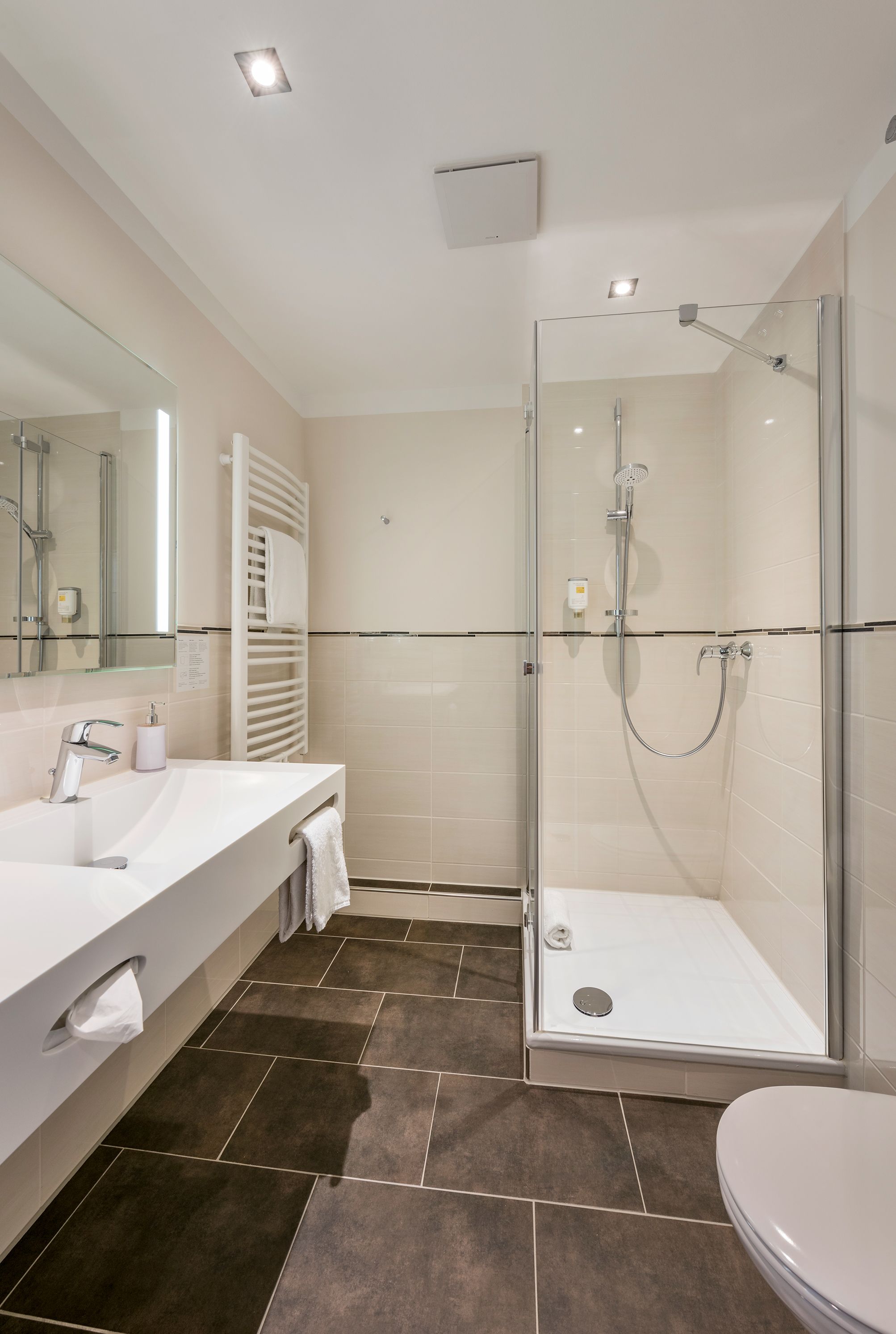 A modern bathroom with a glass-enclosed shower, a white sink, and a large mirror.