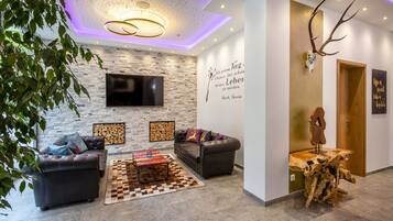 A modern living room with a stone wall, leather sofa, flat-screen TV, and decorative antlers.