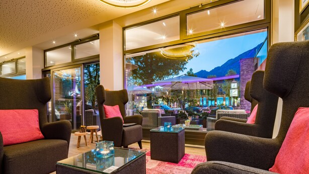 A modern lounge area with comfortable seating, a glass coffee table, and large windows offering a view of the outdoor patio area.