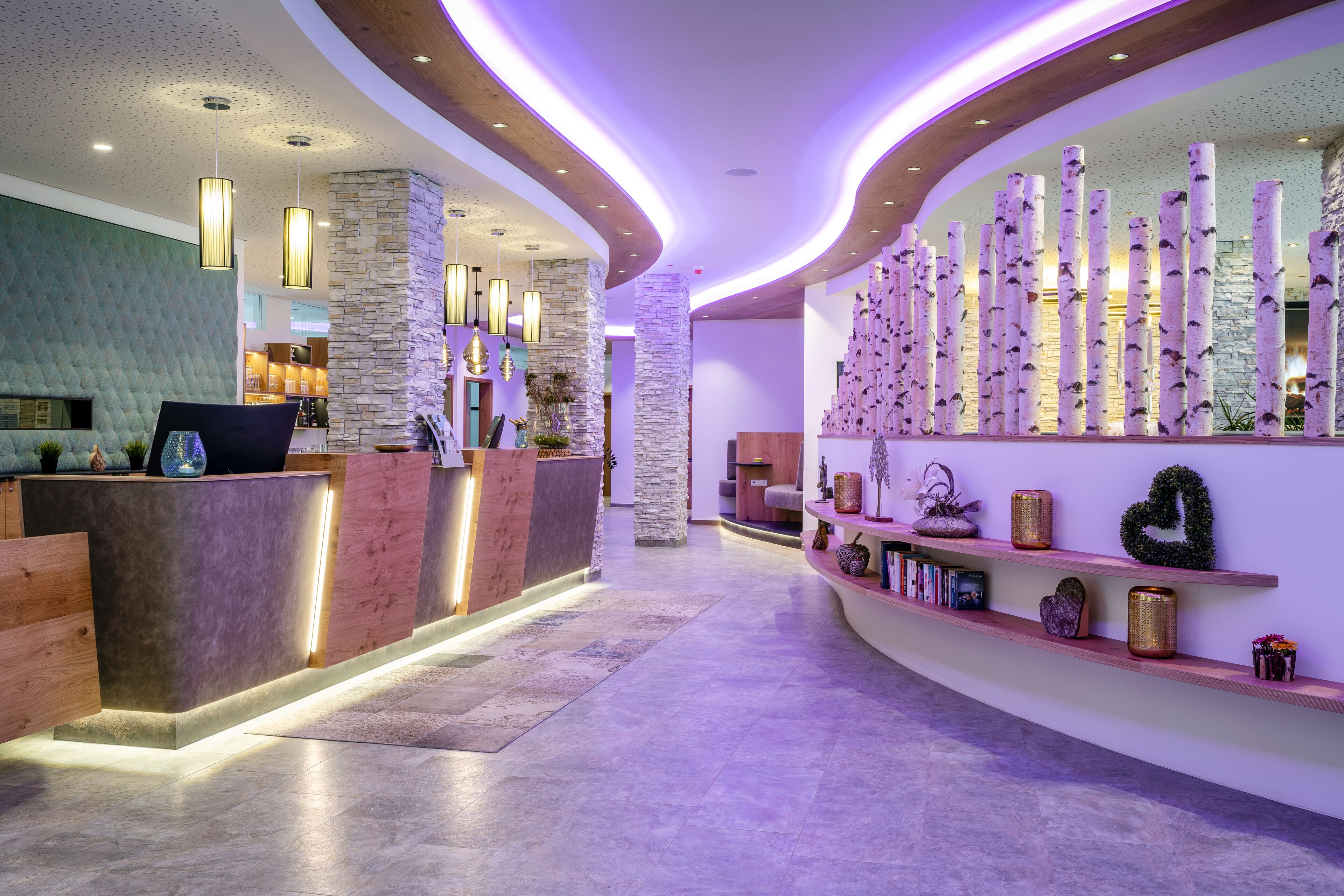 A modern reception area with a curved reception desk, stone pillars, and a wall decorated with vertical elements and shelves with various items.