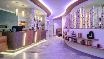 A modern reception area with a curved reception desk, stone pillars, and a wall decorated with vertical elements and shelves with various items.