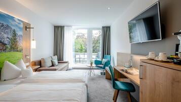 Et hotelværelse med seng, skrivebord, fjernsyn, balkon med udsigt til bjergene og et billede på væggen.