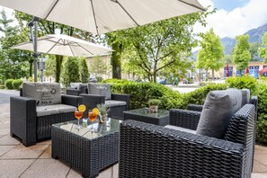 An outdoor seating area with wicker furniture, a glass table, and a large umbrella.