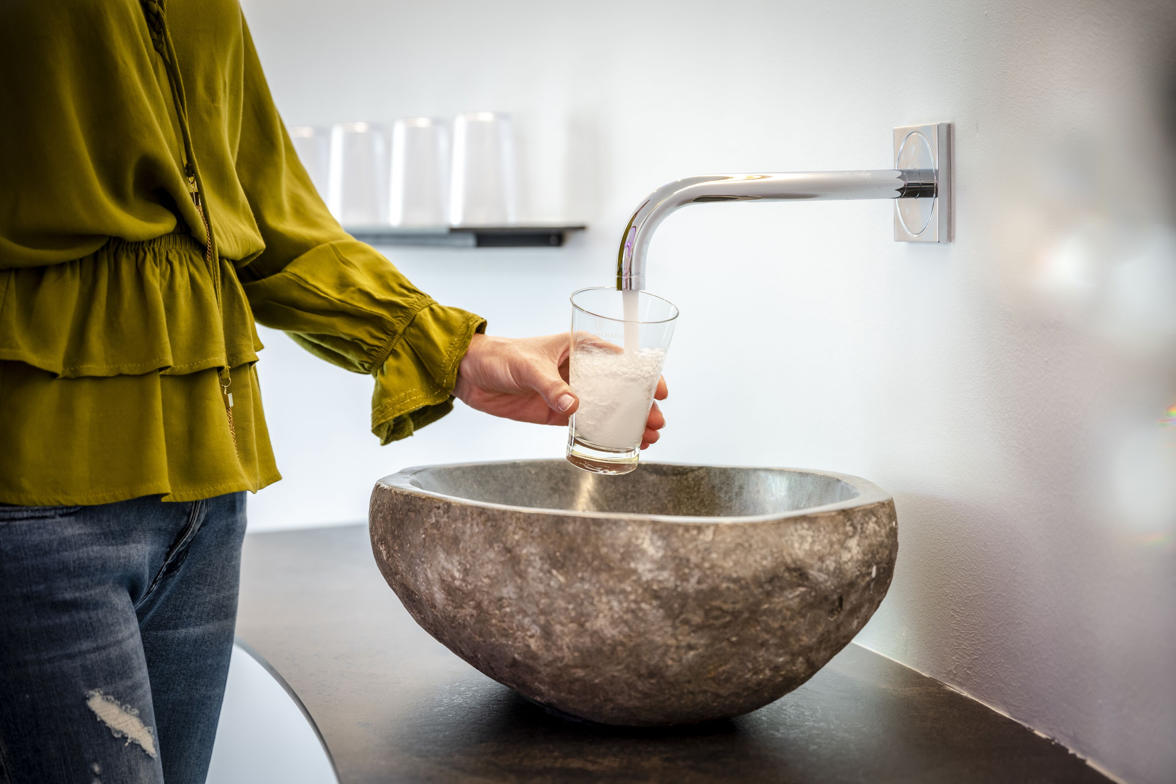 Eine Person gießt eine weiße Flüssigkeit aus einem Glas in ein großes, rundes Becken aus Stein.
