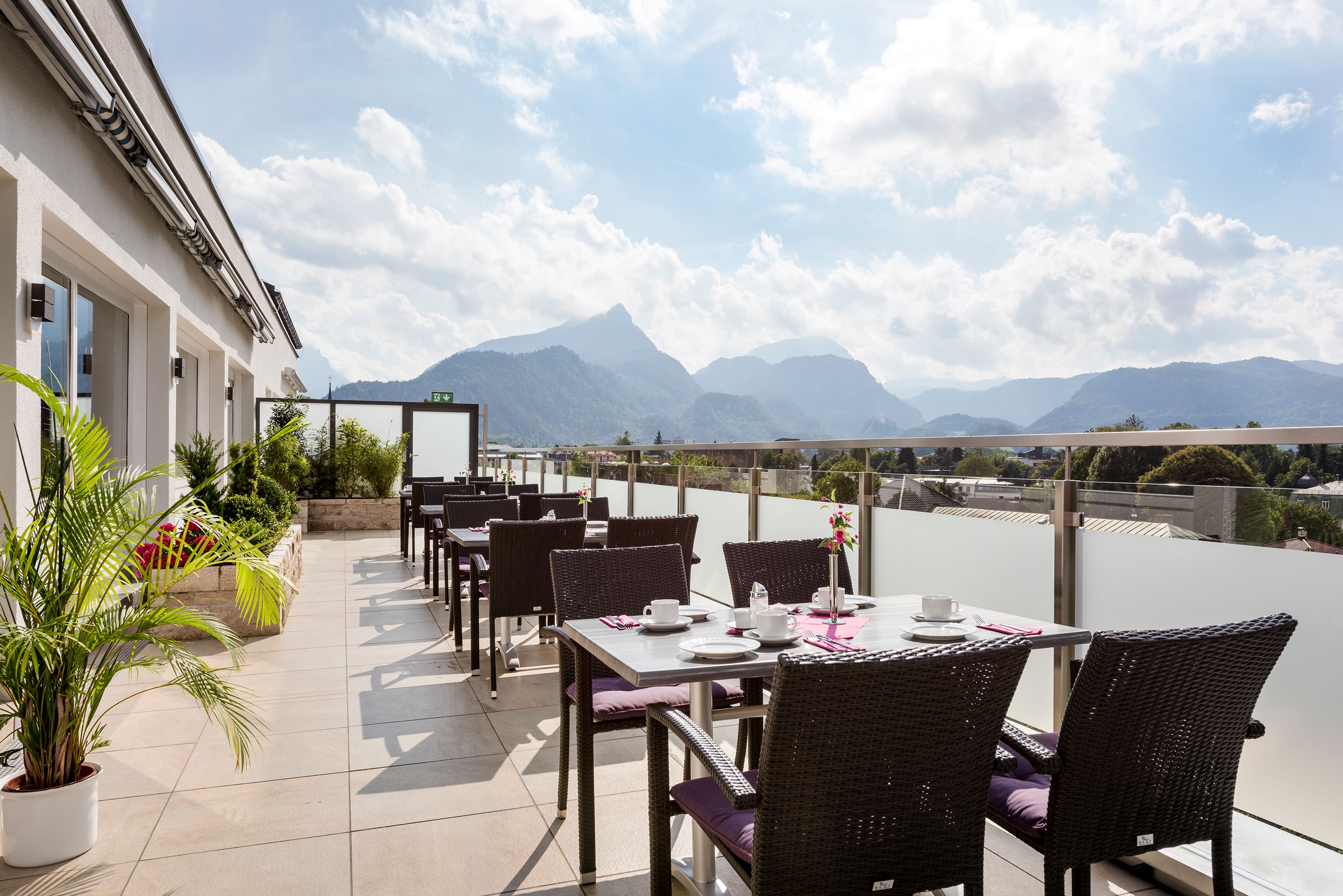 An outdoor dining area with tables and chairs, a potted plant, and a view of mountains.