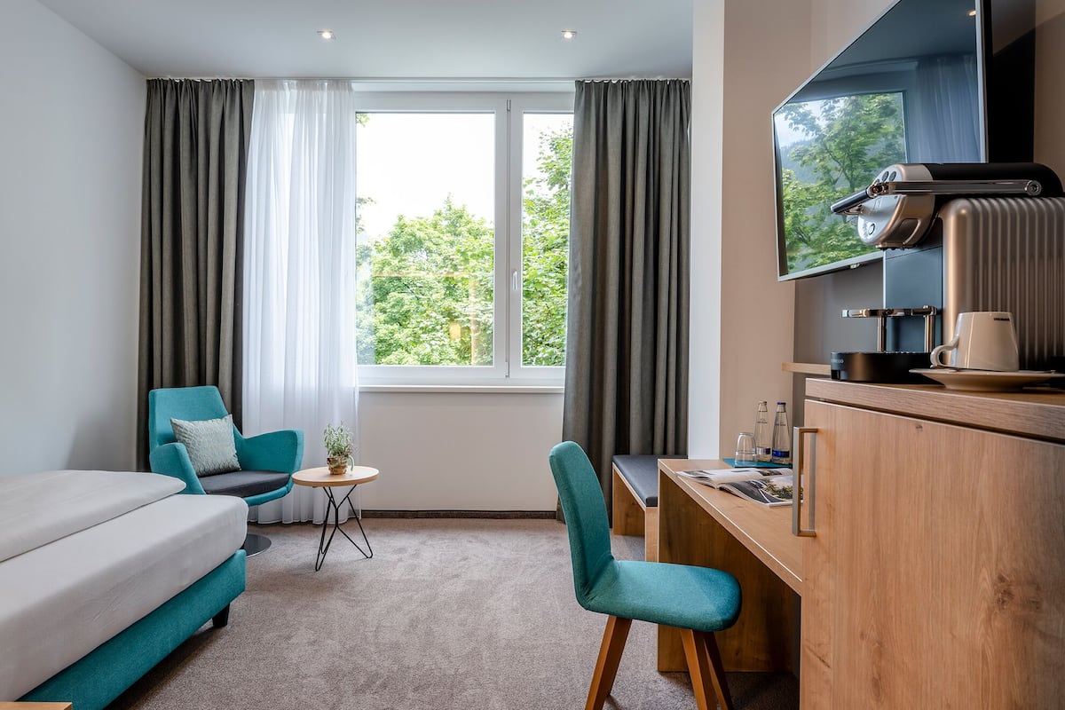 A hotel room with a sofa, a desk, a chair, a TV, and a window with curtains.
