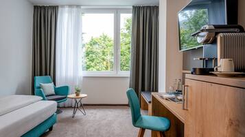 A hotel room with a sofa, a desk, a chair, a TV, and a window with curtains.