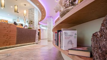 A modern reception area with a wooden reception desk, a curved bookshelf with books, and a stone pillar.