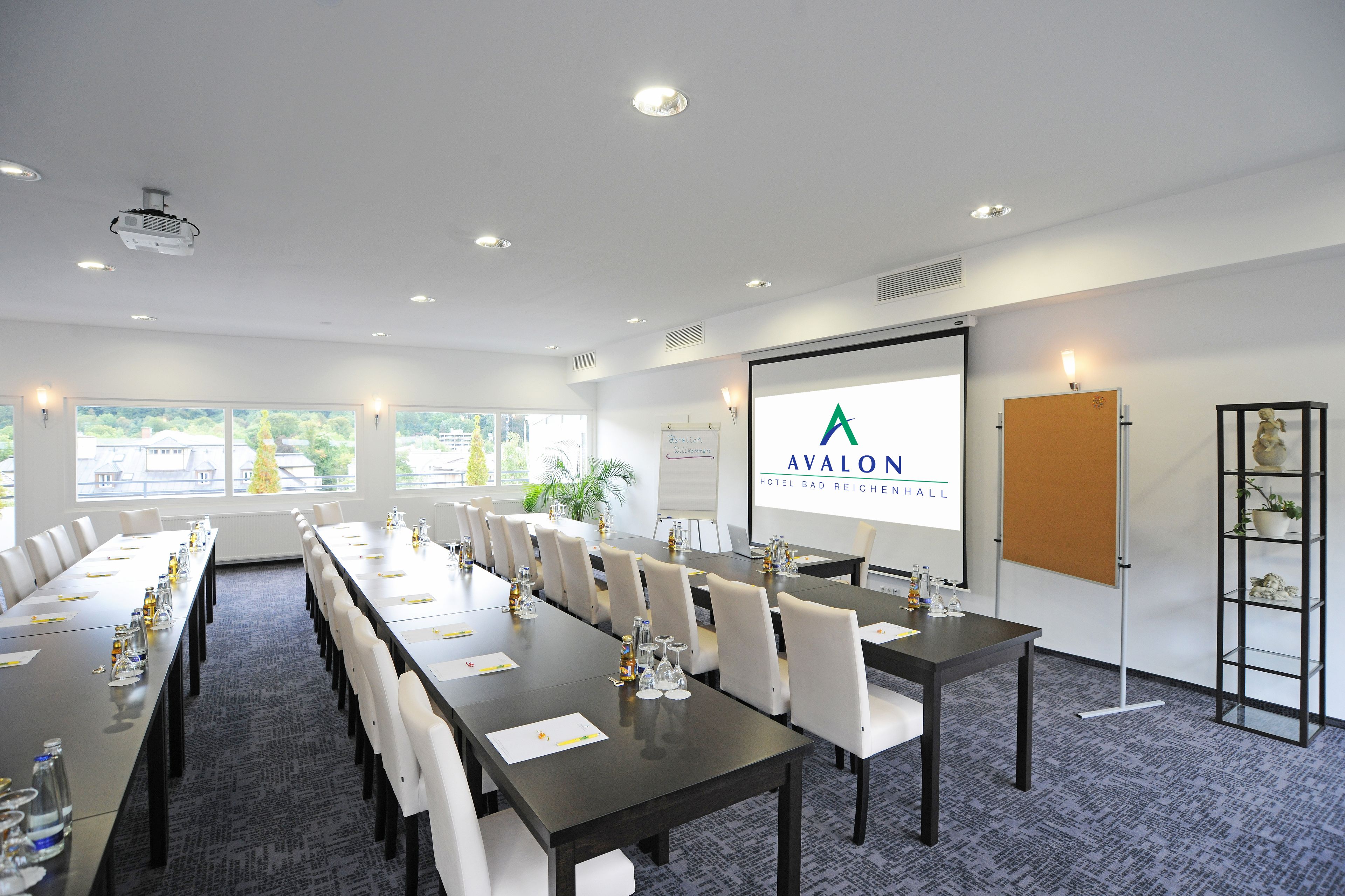 Une salle de conférence avec une longue table, des chaises blanches, un écran de projection et un tableau blanc.