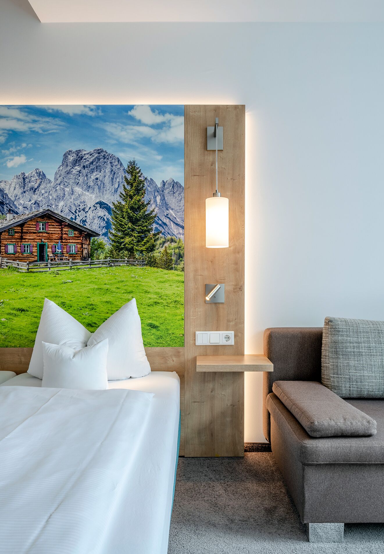 Una habitación de hotel con una cama, un sofá, una lámpara de pared y un mural de un paisaje montañoso.