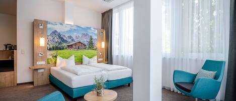A hotel room with a bed, a desk, a chair, and a painting of a mountain landscape.