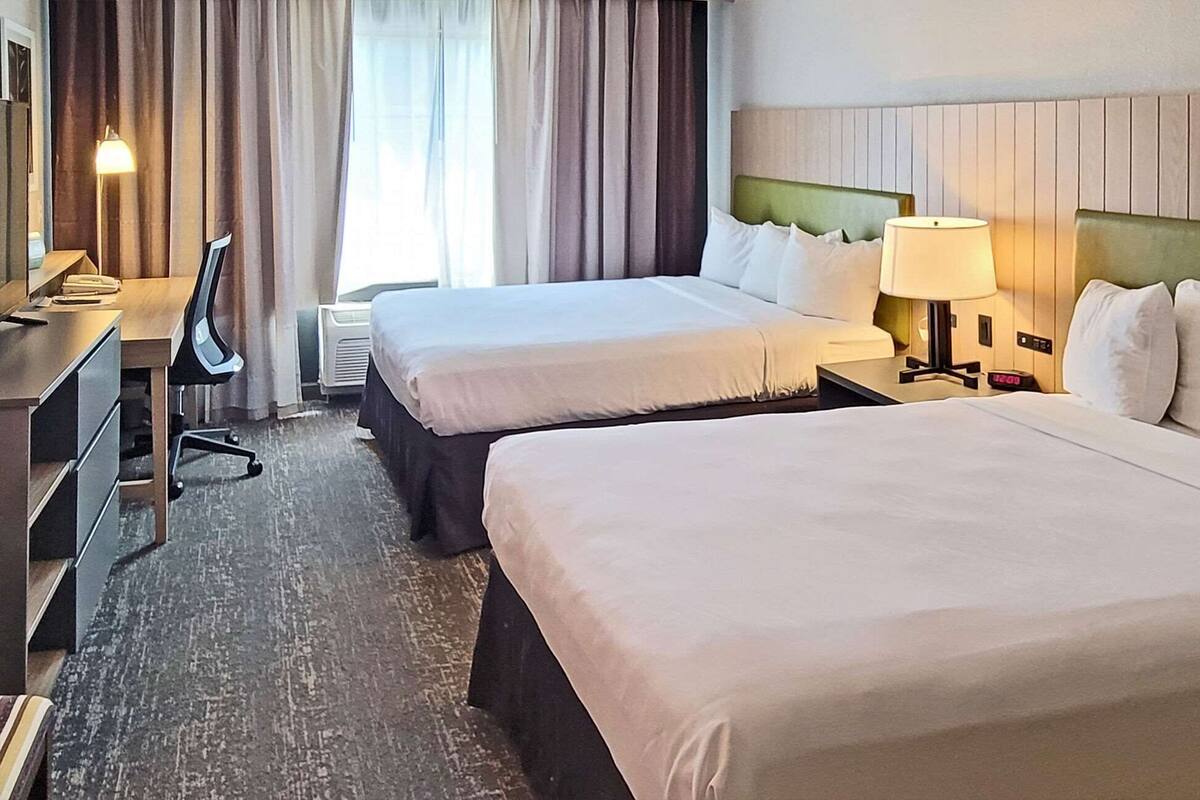A hotel room with two beds, a desk, a chair, and a lamp.