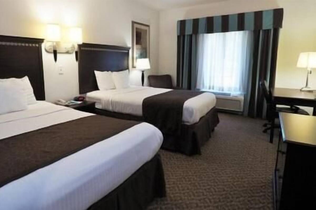 A hotel room with two beds, a desk, and a chair.