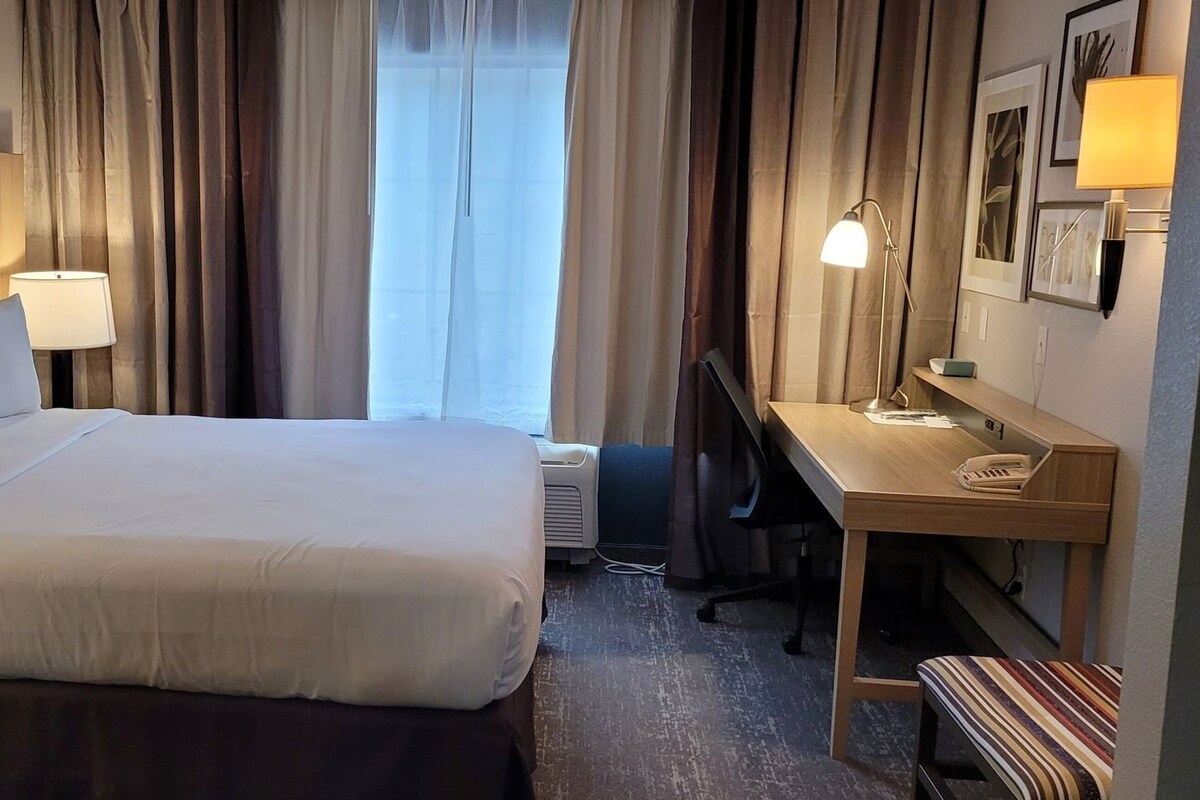 A hotel room with a bed, desk, chair, and a window with curtains.