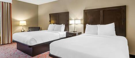 A hotel room with two beds, a patterned carpet, and a nightstand with a lamp.