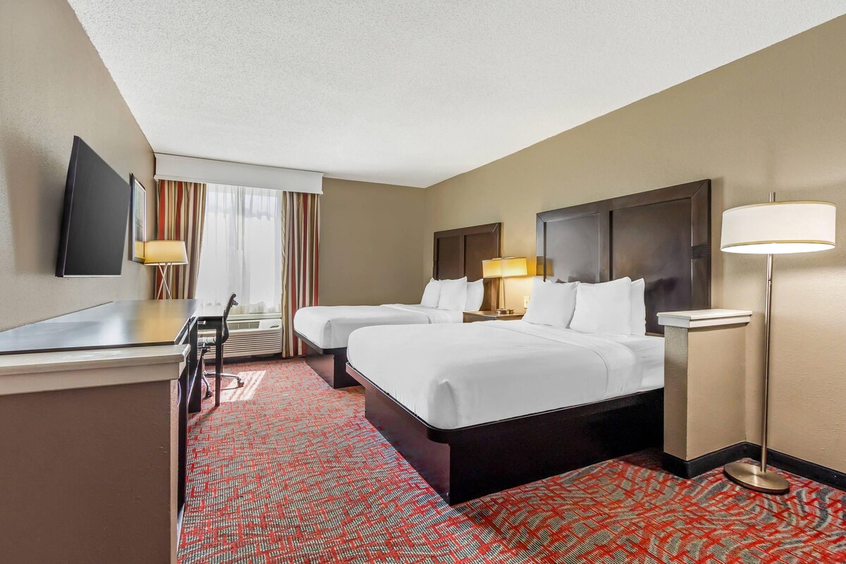 Habitació d'hotel amb dos llits, un escriptori, un televisor i una làmpada.