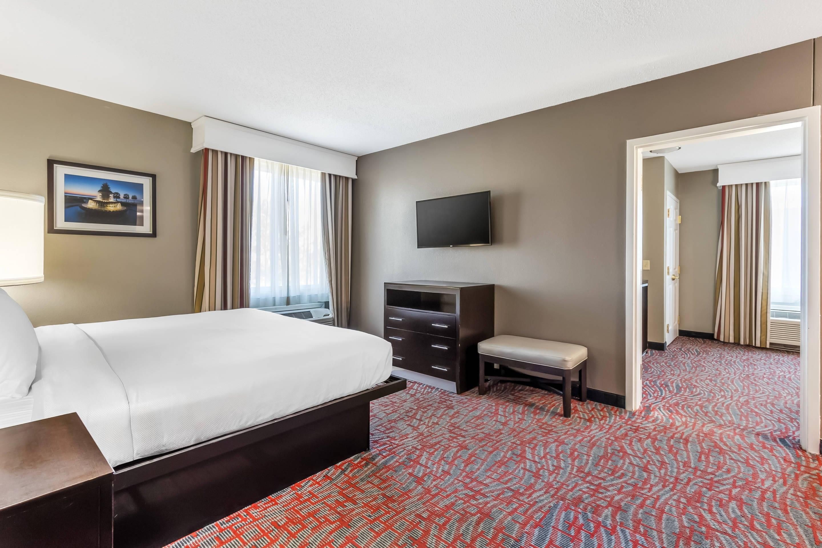 A hotel room with a bed, a TV, a desk, a chair, and a patterned carpet.