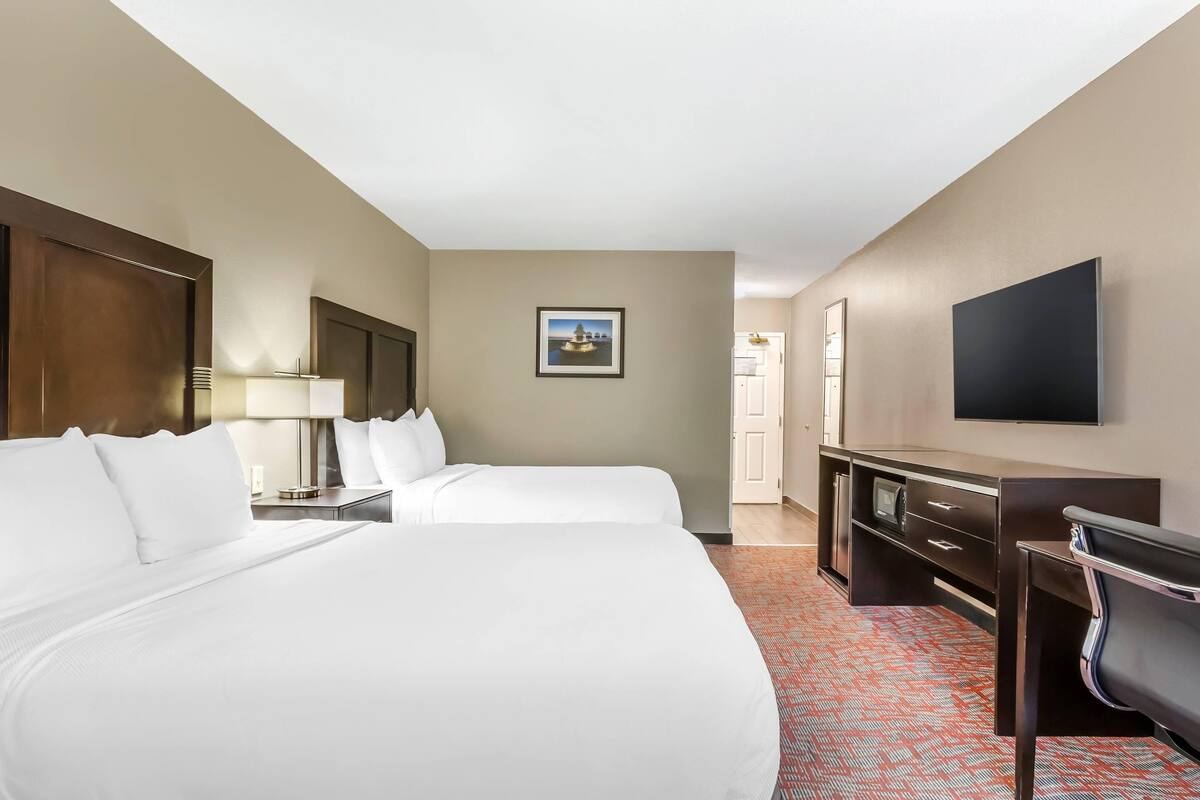A hotel room with two beds, a desk, a TV, and a framed picture on the wall.