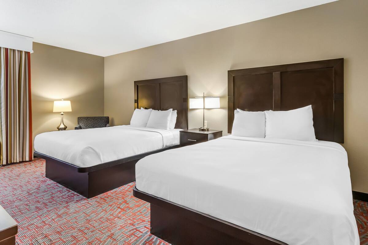 A hotel room with two beds, a patterned carpet, and a nightstand with a lamp.