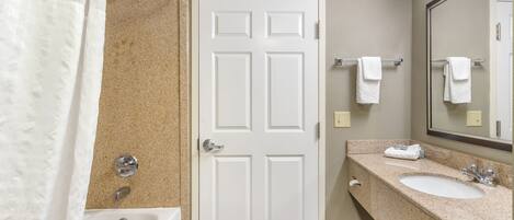 A bathroom with a white door, a bathtub, a sink with a mirror, and a towel rack.