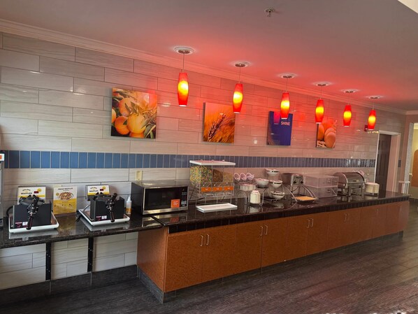 Un área de cocina moderna con estación de café, máquina para gofres, microondas y diversos electrodomésticos.