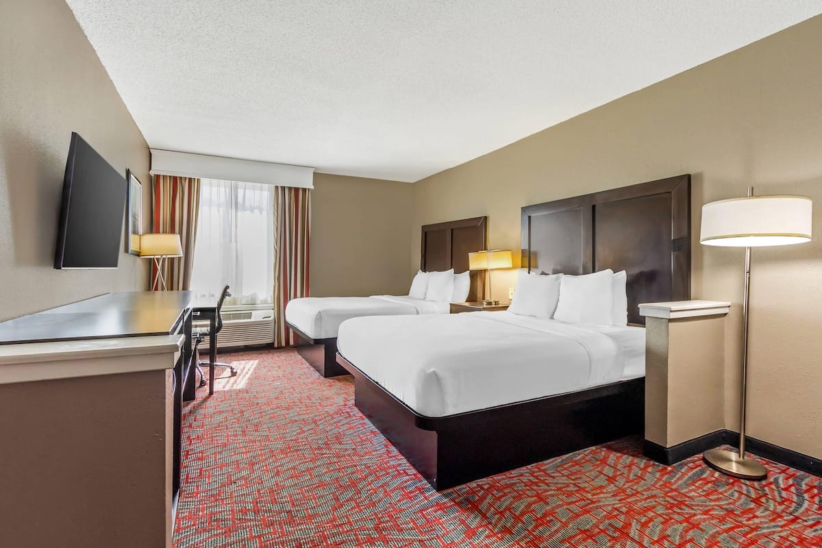 A hotel room with two beds, a desk, a TV, and a lamp.