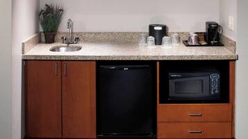 A compact kitchen with a granite countertop, stainless steel sink, black dishwasher, and a microwave.